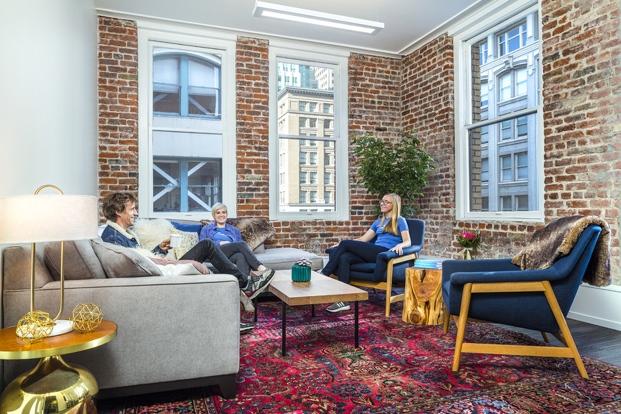 inside office view of three people sitting by a exposed brick wall corner with big windows