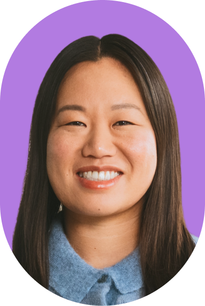 Smiling woman with straight dark hair, wearing a blue collared top, in front of a solid purple background, exuding confidence in an AI-inspired setting.