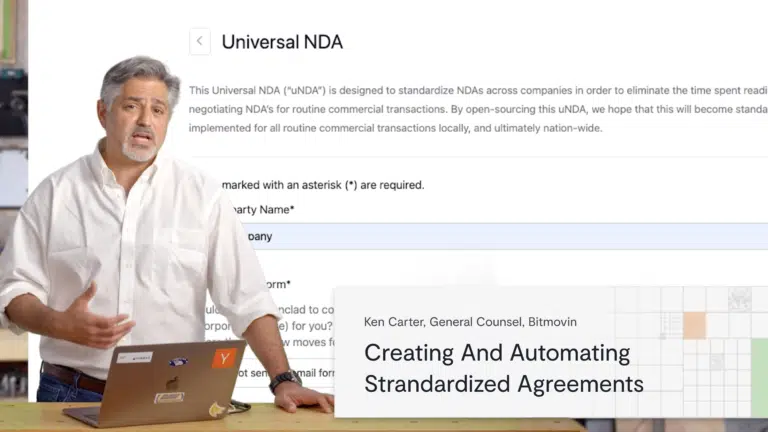 A man stands next to a desk with a laptop, presenting in front of a screen displaying a Universal NDA form. Onscreen text reads: Ken Carter, General Counsel, Bitmovin—contract masters creating and automating standardized agreements.