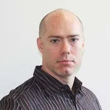 A man with a shaved head wearing a dark, striped collared shirt looks directly at the camera against a plain, light-colored background, evoking the professionalism you'd expect from a LinkSquares alternative.