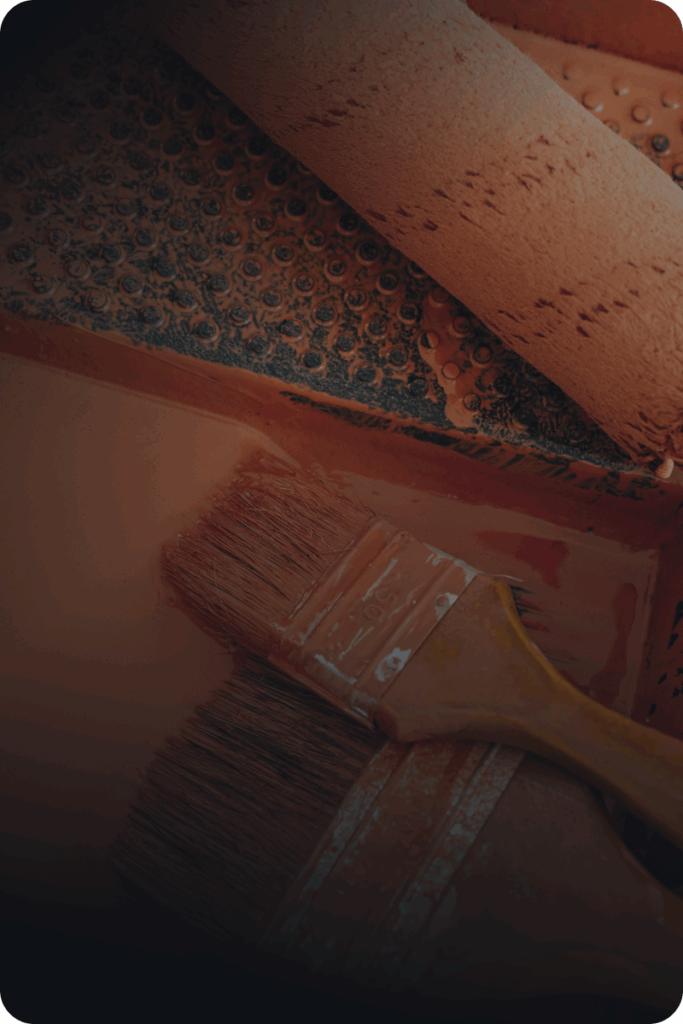 Two paintbrushes and a paint roller rest in a paint tray filled with brown paint, ready for ironclad customers to tackle their next painting project.