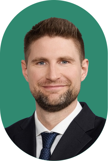 A man with short brown hair and a trimmed beard, wearing a dark suit, white shirt, and navy tie, smiles in front of a green background—projecting confidence in contract intelligence.