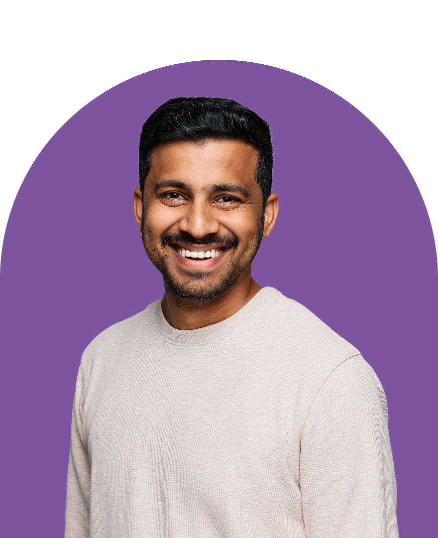 Get a Custom Demo A man with short dark hair and a beard is smiling, wearing a light beige sweater. The background is white with an ironclad purple arch shape behind him.