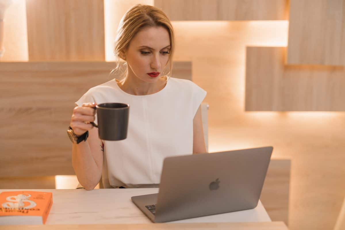 person in white sitting in front of a laptop, holding a mug