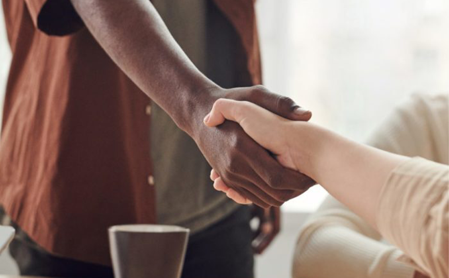 Standing person shakes the hand of a person sitting across a desk | Negotiating SaaS Contracts