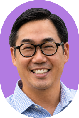 A smiling man with short dark hair and glasses, wearing a light blue checkered shirt, is shown against a purple oval background, evoking the approachable face of AI innovation.