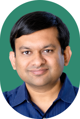 A man with short black hair and wearing a blue collared shirt is smiling in front of a green background, giving the impression of someone engaged with AI technology.