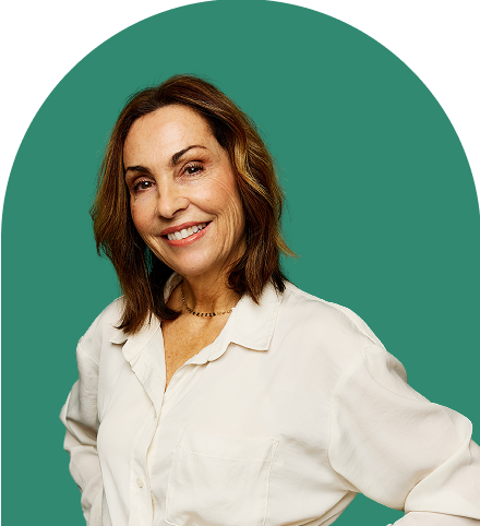 A woman with shoulder-length brown hair smiles while standing against a green background, ready to present ironclad product videos. She is wearing a white button-up shirt and a necklace.