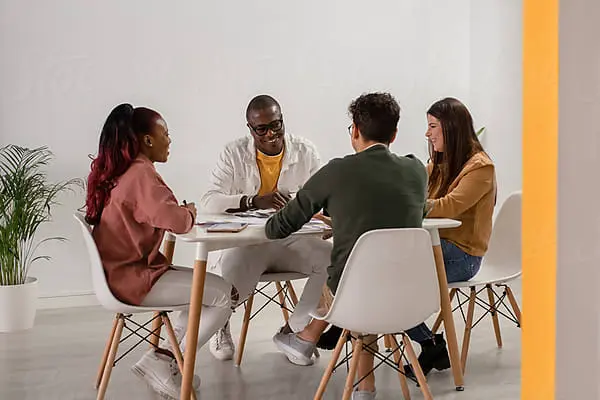 group of four people sitting around a square table in white chairs