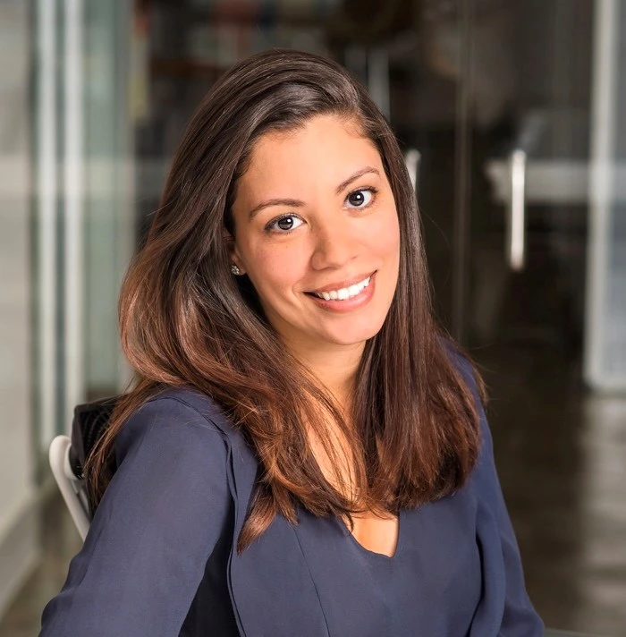 A woman with long brown hair and a navy blouse sits smiling in a modern office with glass walls, suggesting a friendly workplace—perfect for teams seeking a Lexion alternative.