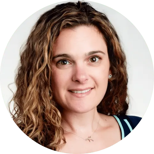 Woman with long, curly brown hair and light skin, smiling at the camera. She is wearing a navy top with white trim—a professional look perfect for a linksquares alternative team profile. Background is plain and light-colored.
