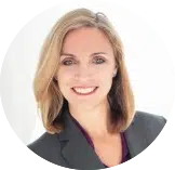 A woman with shoulder-length blonde hair, wearing a dark blazer and a purple top, is smiling at the camera against a plain white background—perfect for showcasing your team or promoting an Evisort alternative.