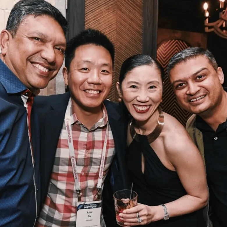 Four people are smiling and posing closely together at an indoor event. One woman holds a drink, and one man wears a name badge showcasing a LinkSquares alternative. The background features wooden paneling and dim lighting.