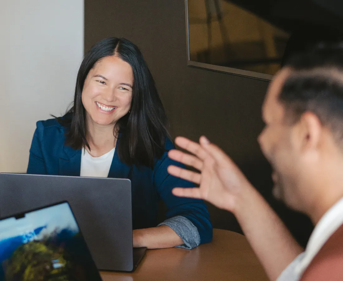 two people smiling at each other in front of their laptops