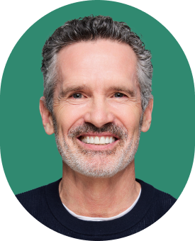 Smiling middle-aged man with short gray hair and a beard, wearing a dark sweater, posing in front of a plain green background.