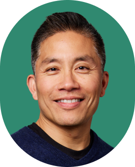 Smiling man with short, dark hair wearing a navy blue sweater, pictured against a green background.