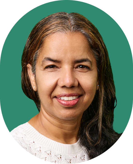 Smiling woman with long, dark hair and gray streaks, wearing a white knit sweater, in front of a solid green background.