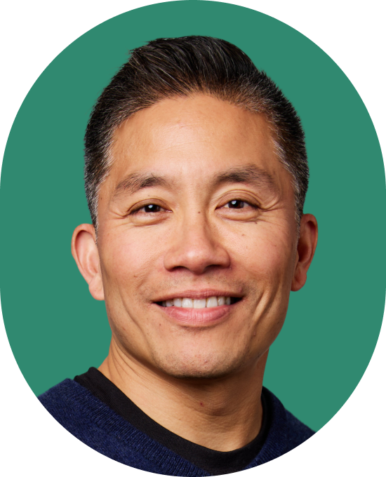 A man with short dark hair and a friendly smile, wearing a navy sweater, is shown against a solid green background.