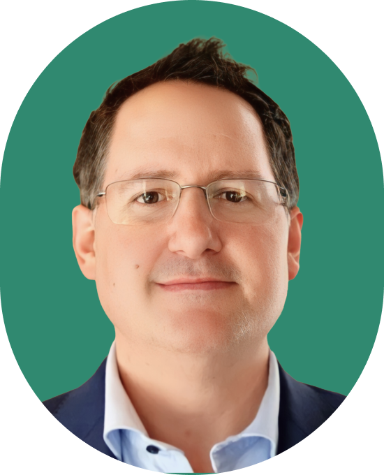 A man with short dark hair and glasses, wearing a blue blazer and light blue shirt, poses in front of a solid green background.