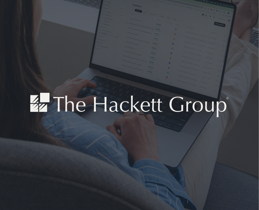 A person in striped pajamas uses a laptop, with The Hackett Group logo and name overlaid in the center of the image.