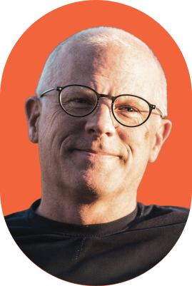 Smiling middle-aged man with short gray hair and round glasses wearing a black shirt, depicted against an orange oval background—portraying the confidence of an ironclad jurist AI.