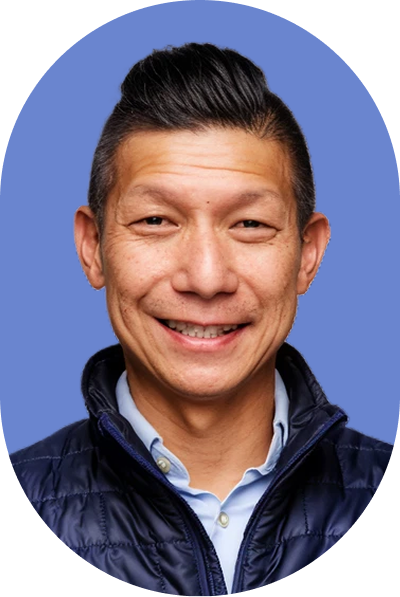 Smiling man with short dark hair wearing a blue quilted jacket over a light blue shirt, posed in front of a solid blue background with an oval white frame, evoking a modern and approachable look ideal for AI professionals.