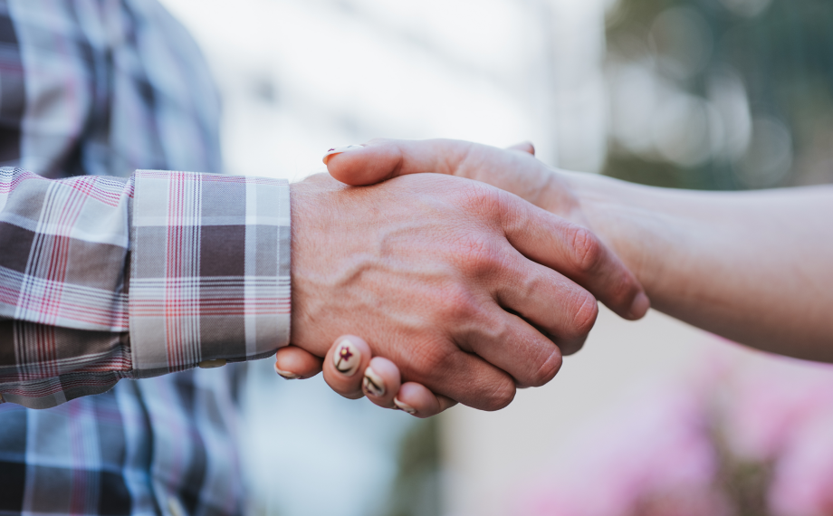 Close-up of two people shaking hands outdoors, one wearing a plaid shirt and the other with painted nails—an ideal visual for illustrating procurement AI effective use cases in forging collaborative business partnerships.